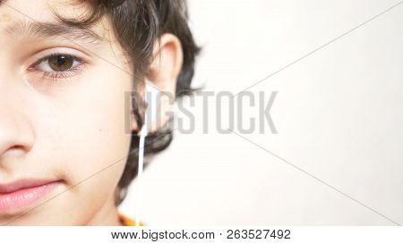 The Teenager Puts On White Headphones And Listens To Music. Close-up Of Half A Face. Copy Space.