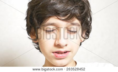 A Young Boy Looks At The Camera And Smiling. The Boy Laid His Head On His Palm And Looked Into The C