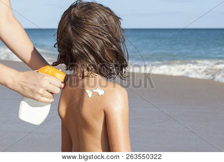 Mother Applying Sunblock Cream With Spray Gun To Her Daughter On Back. Idyllic Beach Background