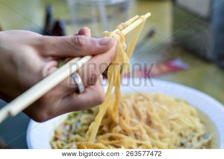 Chopsticks Lifting Up Hot Noodles In A Peanut Butter Sauce.  Noodles In A Chinese Restaurant.