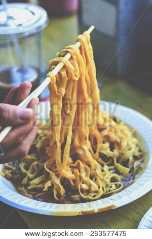 Chopsticks Lifting Up Hot Noodles In A Peanut Butter Sauce.  Noodles In A Chinese Restaurant.