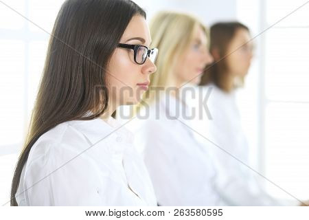 Attractive Businesswoman At Meeting Or Conference Against The Background Of Colleagues. Group Of Bus