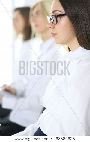 Attractive Businesswoman At Meeting Or Conference Against The Background Of Colleagues. Group Of Bus