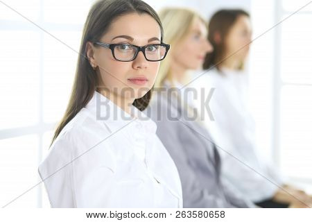 Attractive Businesswoman At Meeting Or Conference Against The Background Of Colleagues. Group Of Bus