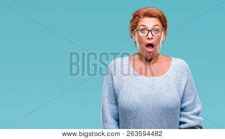 Atrractive senior caucasian redhead woman wearing glasses over isolated background afraid and shocked with surprise expression, fear and excited face.