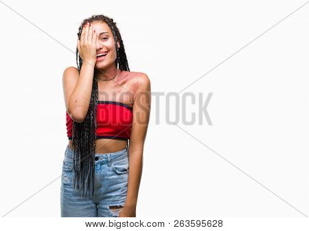Young braided hair african american with pigmentation blemish birth mark over isolated background covering one eye with hand with confident smile on face and surprise emotion.