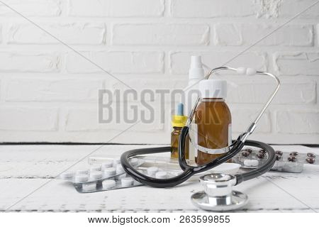 Close Up View Over A White Wooden Table With Syrip, Pills, Capsules, Sprays, Stethoscope And Thermom