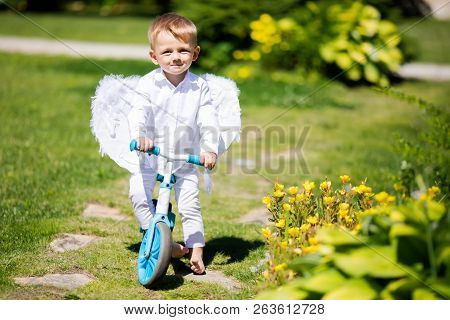 Toddler Boy Wearing Angel Wings Riding A Balance Bike (run Bike), Learning To Keep Balance On A Trai