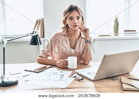 Concentraiting On Project. Beautiful Young Woman In Smart Casual Wear Holding A Cup Of Coffee And Lo