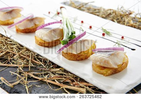 Herring Canape with Potato and Onion on Natural Rustic Background. Beautiful Creative Sea Food Design of Fish Fillet with Scallions on Dry Hay and Black Slate