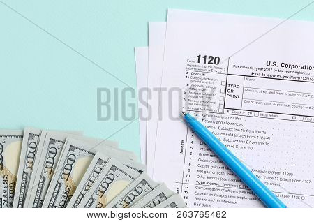 1120 Tax Form Lies Near Hundred Dollar Bills And Blue Pen On A Light Blue Background. Us Corporation
