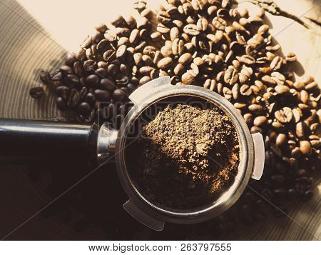 Close Up Of A Metal Portafilter Filled With Coffee Powder And Coffee Beans Around On Wooden Table