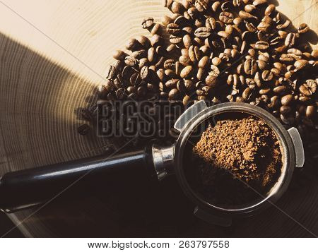 Close Up Of A Metal Portafilter Filled With Coffee Powder And Coffee Beans Around On Wooden Table