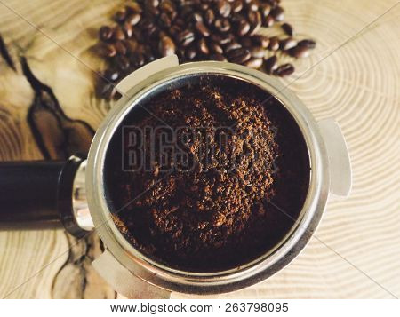 Close Up Of A Metal Portafilter Filled With Coffee Powder And Coffee Beans Around On Wooden Table