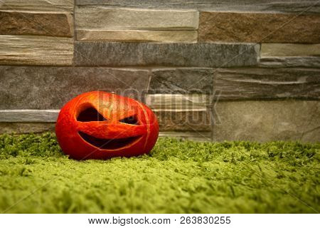 Halloween Pumpkin Stands On A Green Carpet Against A Stone Wall. Jack O` Lantern