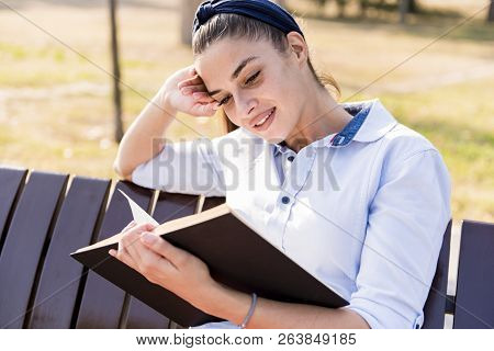 Beautiful  Young Woman  Holding  Open Book And Reading On Bench In Autumn Park