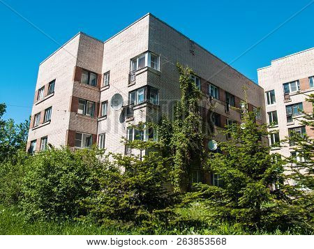 A Five-storey House Of Light Brick Against A Blue Sky With Lush Blooming Greenery Near The Basement 