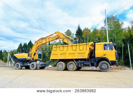 The Wheel Excavator Loads The Earth With A Bucket To The Body Of A Multi-ton Dump Truck On The Const