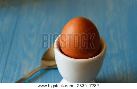 Boiled Egg In A White Egg Cup With Spoon On A Blue Background