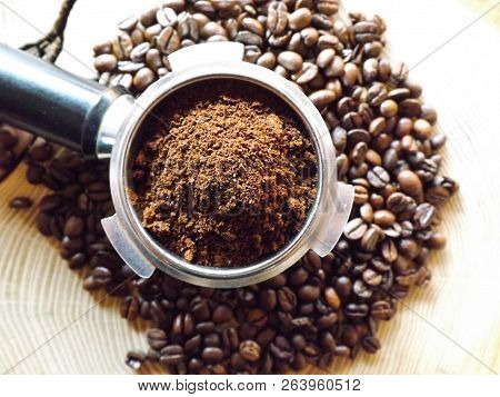 Close Up Of A Metal Portafilter Filled With Coffee Powder And Coffee Beans Around On Wooden Table