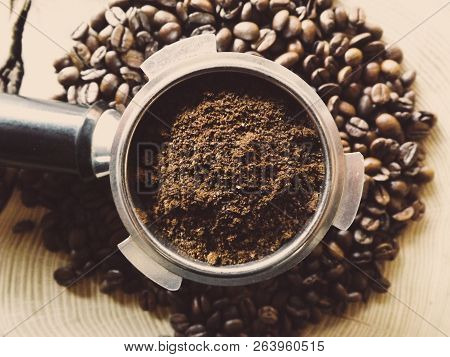 Close Up Of A Metal Portafilter Filled With Coffee Powder And Coffee Beans Around On Wooden Table