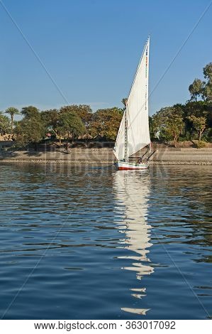 Traditional Egyptian Felluca River Boat Sailing On The Nile With Reflection In Water