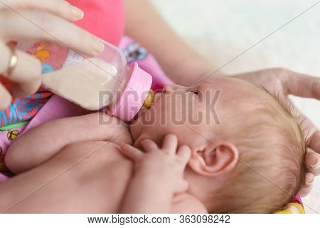 A Small Newborn Girl Is Fed Formula From A Bottle In Her Mothers Arms. Artificial Feeding