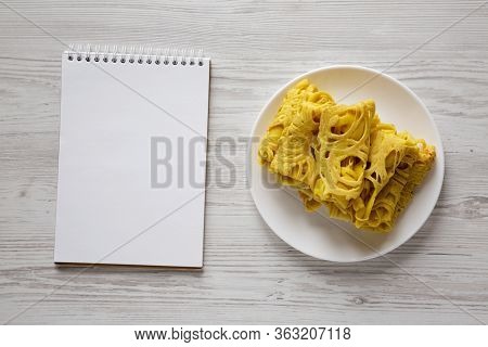 Homemade Net Crepe Roti Jala On A White Plate, Blank Notepad On A White Wooden Background, Top View.