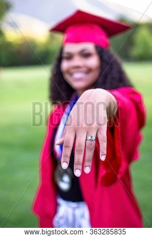 Multiethnic woman in her graduation cap and gown showing her class ring. Selective focus on the hand and ring. Way to go. Great Job Graduate!