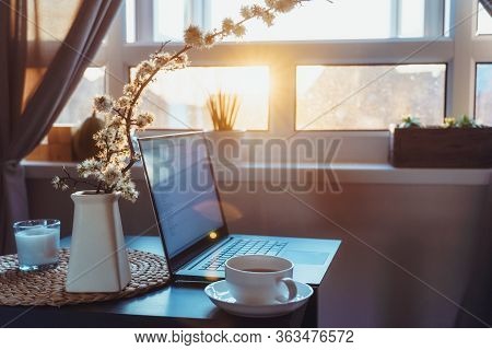 Home Work Place With Laptop, Cup Of Hot Drink And Blooming Brunch In Vase On Coffee Table Near Windo