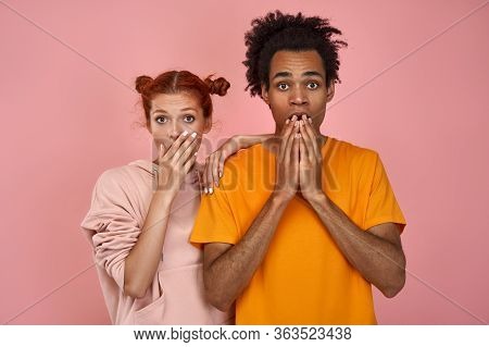 Frightened Young Red Haired Girlfriend And Dark Skinned Boyfriend Cover Mouths With Hands, Keep Eyes