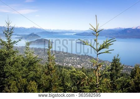 A Hill On A Sunny Day. The Nahuel Huapi Lake Is Below. Rocks And Pine Trees Accompany The View.