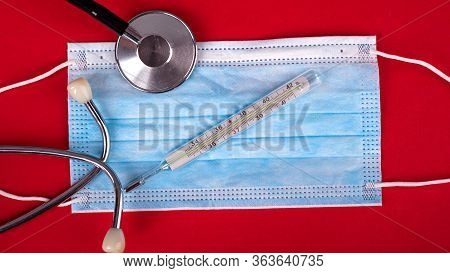 Statoscope Thermometer And Medical Disposable Mask On A Red Background Top View Close-up. Covid-19 I