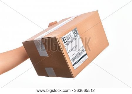 Hand of caucasian young man holding cardboard package showing label with codebar over isolated white background