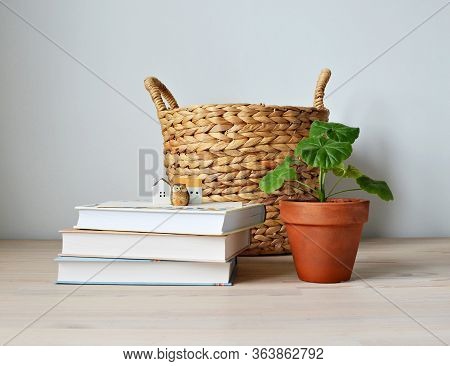 Wicker Basket, Houseplant Pelargonium In Terracotta Pot, Books, Ceramic Houses, Owl And Wooden Desk 