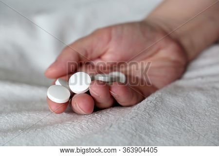 White Pills In A Palm Of Female Hand On The Bed. Concept Of Medication, Vitamins Or Sleeping Pill