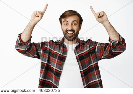 Entusiastic Bearded Man Pointing Fingers Up, Smiling Amazed, Showing Advertisement, Standing In Chec