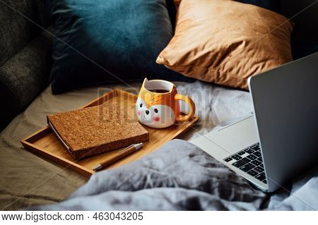 Cozy Home, Autumn Warm Mood. Laptop, Notebook And Cup Of Tea At Tray On Blanket In Bed In The Interi