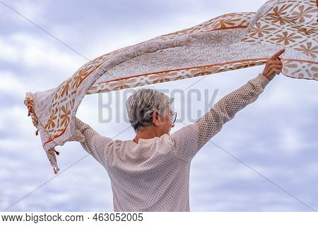 Rear View Of Senior Caucasian Woman Short Hair Standing Face To The Sea With Outstretchedd Arms Wavi