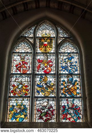 Germany, Lubeck - July 13, 2022: Heiligen Geist Hospital. Many Coat Of Arms On Stained Window Street