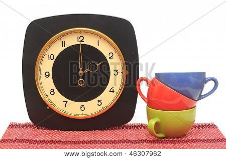 Set van kleurrijke kopjes met oude muurklok op wit. Tea time