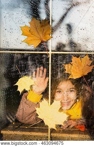 Child Looks Out Of The Window Of The House Outside, Autumn Weather, Wet Glass With Drops After Rain,