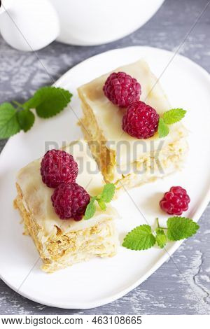 Pieces Of Napoleon Cake Decorated With Raspberries And Lemon Balm Leaves On A Light Background.