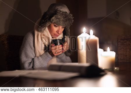 Freezing Young Woman In Winter Clothes Warms Her Hands On Cup Of Tea And Lights With Candles As Ener