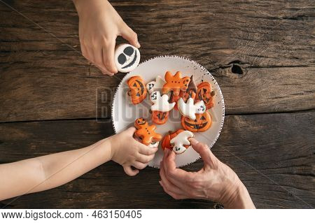Childrens Hands Reach For Handmade Edible Gingerbread On Plate. Top View. Halloween Pumpkin, Ghosts 