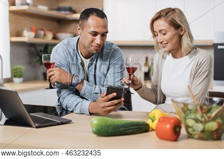 Distracted From Cooking Happy Young Multinational Family Couple Using Cellphone Checking Interesting