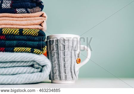 Stack Of Folded Woolen Checked Blankets And Mug In Wollen Cover, Autumn And Cold Winter Concept
