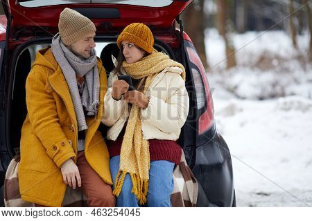 Portrait Of Young Couple Sitting In Car Trunk In Winter Forest While Enjoying Travel For Holidays, C