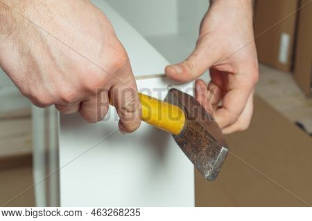 Male Hands Hold Metal Hammer With Yellow Plastic Handle, Driving Dowel, Assembling White Drawer Of D