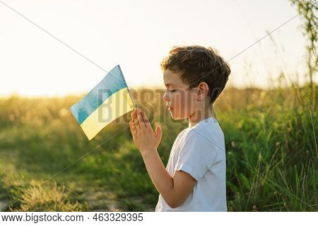 Ukrainian Boy Closed Her Eyes And Praying To Stop The War In Ukraine In A Field At Sunset. Hands Fol